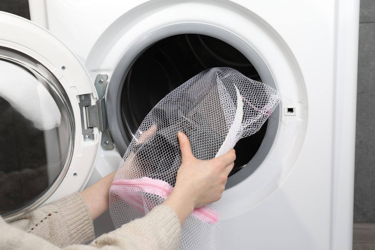 Schuhe können in der Waschmaschine sehr laut sein. - ein Waschsack kann den Geräuschpegel etwas senken Frau legt in Waschsack verpackte Schuhe in Waschmaschine - Dürfen Stoffschuhe in die Waschmaschine?