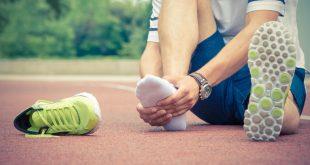 Person hält sich schmerzenden Vorderfuß. Daneben liegt ein Laufschuh