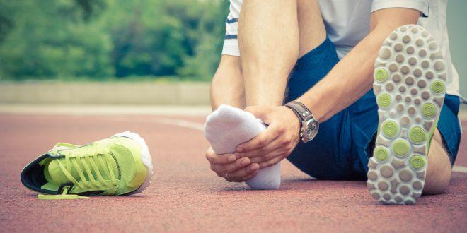 Person hält sich schmerzenden Vorderfuß. Daneben liegt ein Laufschuh