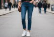 Junge Frau trägt weiße Ralph Lauren Sneaker mit Jeans und blauem Pullover in urbaner Umgebung